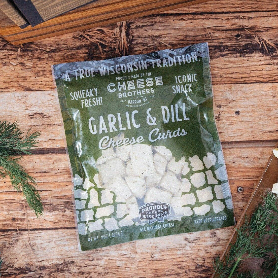 Packaged garlic and dill cheese curds on a wooden surface with fresh herbs.