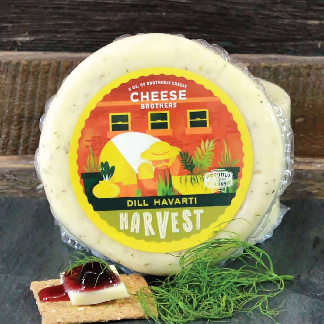 Dill Havarti cheese wheel with a label on a slate board against a wooden background