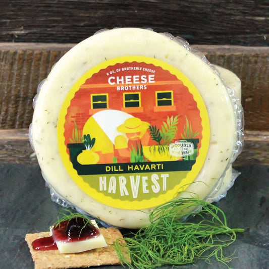 Dill Havarti cheese wheel with a label on a slate board against a wooden background