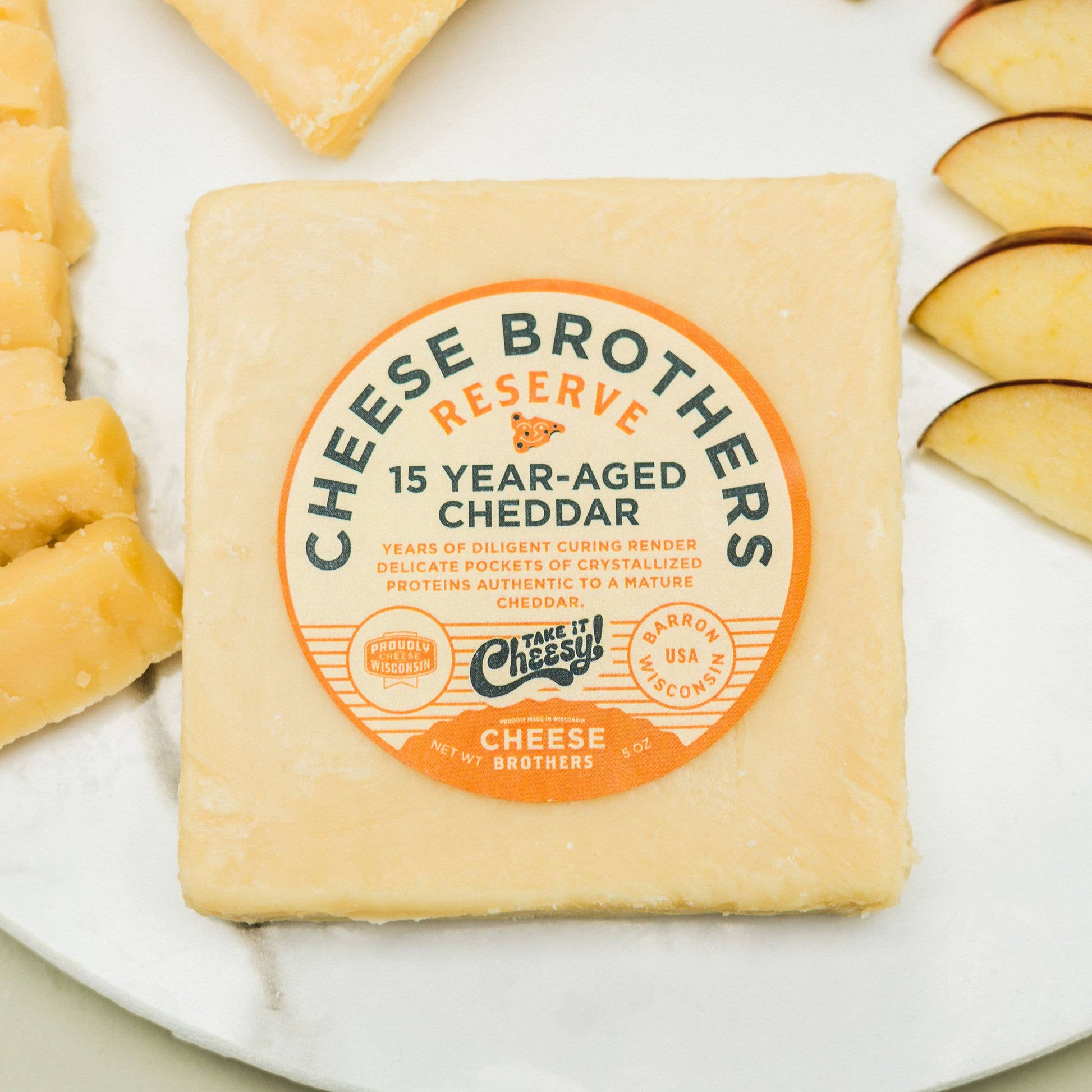 Block of Cheese Brothers Reserve 15 Year-Aged Cheddar with cheese sticks and apple slices on a plate.