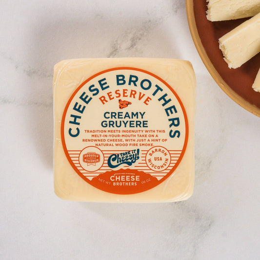 Block of Cheese Brothers Creamy Gruyère cheese on a marble surface with sliced bread.